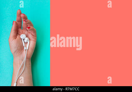 Trendy lebende Korallen Hintergrund. Lady's Hand mit schönen Maniküre holding Ohrhörer auf Türkis und Koralle Farbe Hintergrund. Stockfoto