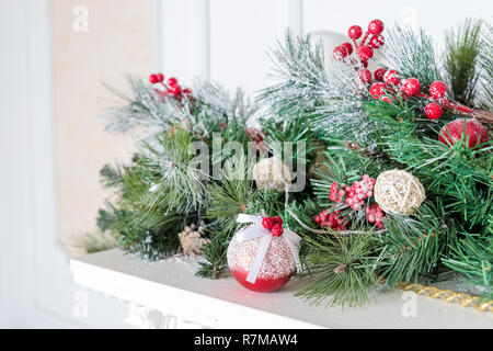 Weihnachtsdekoration von Holly Berry und Pine Cone. Weihnachten Hintergrund. Grüne Zweige mit roten Beeren. Home Decor für Feiertage. Deko Kugeln mit Tannenzapfen und Tannenzweigen, weiße Kerze. Stockfoto