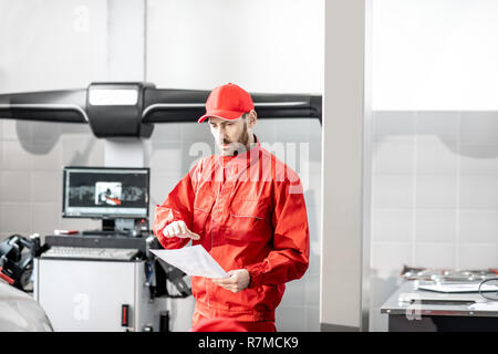Automechaniker in roter Uniform arbeiten mit Computer, Rad Allignment am Auto Service Stockfoto