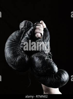 Bis erhobenen Hand der Mann hält ein paar alte schwarz Leder Boxhandschuhe, schwarz hintergrund Stockfoto