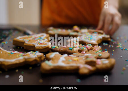 Weihnachtsbäckerei. Freunde verzieren frisch gebackene Lebkuchen Plätzchen mit Puderzucker und Süßwaren Dichtmasse, Ansicht von oben. Festliche Essen, Familie culi Stockfoto