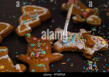 Weihnachtsbäckerei. Freunde verzieren frisch gebackene Lebkuchen Plätzchen mit Puderzucker und Süßwaren Dichtmasse, Ansicht von oben. Festliche Essen, Familie culi Stockfoto