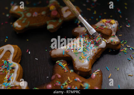 Weihnachtsbäckerei. Freunde verzieren frisch gebackene Lebkuchen Plätzchen mit Puderzucker und Süßwaren Dichtmasse, Ansicht von oben. Festliche Essen, Familie culi Stockfoto