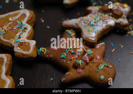 Weihnachtsbäckerei. Freunde verzieren frisch gebackene Lebkuchen Plätzchen mit Puderzucker und Süßwaren Dichtmasse, Ansicht von oben. Festliche Essen, Familie culi Stockfoto