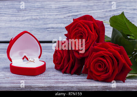 Rote Rosen und Diamond Ring im Karton. Engagement Ring in Herzform, und drei Rosen auf Holz- Hintergrund. Heiratsantrag Konzept. Stockfoto