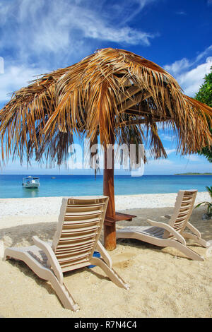 Liegestühle mit strohgedecktem Dach an einem weißen Sandstrand, South Sea Island, Mamanuca, Fidschi. Stockfoto