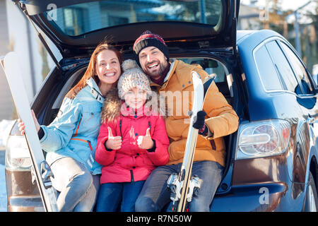 Winter Urlaub. Zeit mit der Familie zusammen im Freien stehen im Kofferraum sitzen mit Skiern Lächeln aufgeregt Mädchen zeigen Daumen hoch Stockfoto