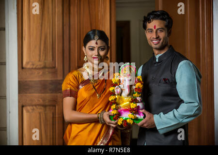 Maharashtrian Paar in traditioneller Kleidung feiern ganapati Festival eine kleine Statue von Lord Ganesha zusammenhalten. Stockfoto