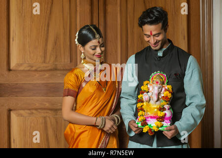 Maharashtrian Paar in traditioneller Kleidung feiern ganapati Festival mit einer kleinen Statue von Lord Ganesha und es zu betrachten. Stockfoto