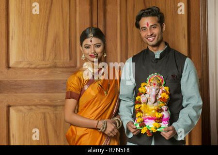 Happy maharashtrian Paar in traditioneller Kleidung feiern ganapati Festival mit einer kleinen Statue von Lord Ganesha. Stockfoto