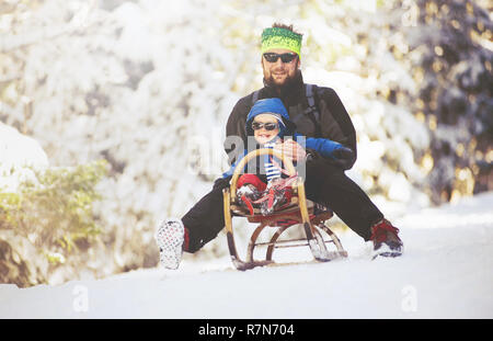 Österreich, Alpen, Februar 2017. Vater und Sohn Spaß durch Bergab auf der hölzernen Schlitten im Winter Natur. Stockfoto