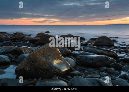 Sonnenuntergang über dem Mull of Galloway aus Machars bouldery Strand an der Küste im Südwesten Schottlands. Stockfoto