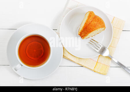 Untertasse mit einem Stück hausgemachten Zitronenkuchen Tasse Tee auf weiße Holztisch. Ansicht von oben. Stockfoto