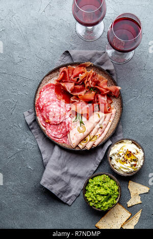Antipasti. Fleischplatte, Chips und Saucen, Rotwein auf grauem Hintergrund. Ansicht von oben Stockfoto