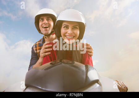 Der junge lächelnde Paar reiten auf einem Motorroller. Stockfoto