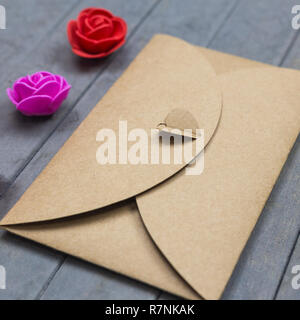 Umschlag aus dem craft-Papier mit Herz und drei kleine Rosen Blumen auf Holz Hintergrund Stockfoto