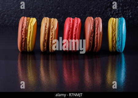 Bunte Dessert bunte Macarons in Pastellfarben auf schwarzem Hintergrund in einer Reihe ausgesetzt. Close-up. Stockfoto