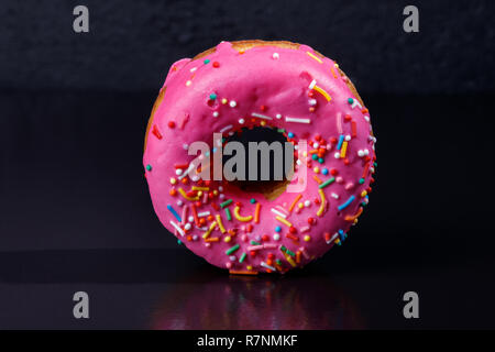 Rosa Donut. Frosted sprengte Donut auf schwarzem Hintergrund. Stockfoto