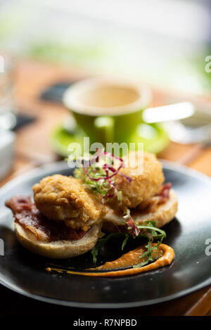 Eier Benedikt mit gebratenen breadcrumb Eier in gerösteten Brötchen mit Schinken und Salat in einem schwarzen Teller. Stockfoto