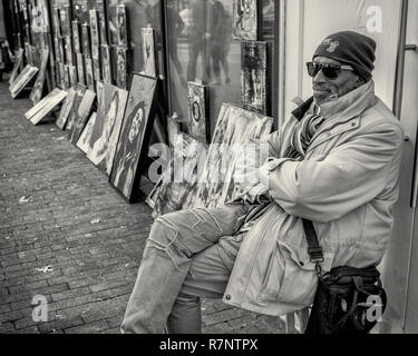 Ein Künstler sitzt mit seinen Gemälden auf der Straße in Harvard Square, Cambridge, MA Stockfoto