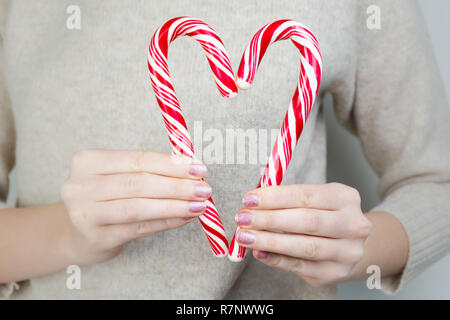 Herz Form von zwei zuckerstangen hergestellt. Liebe Konzept: Frau hält zwei Bonbons Herzen bilden auf Brusthöhe Stockfoto