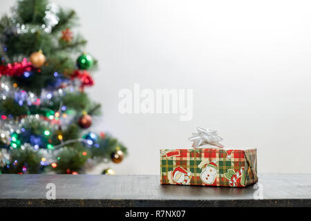 Weihnachtsgeschenk auf Holz Tisch und Kopieren. Vorderansicht des schönen Geschenk und dekorierte Tanne in verschwommenen Hintergrund Stockfoto