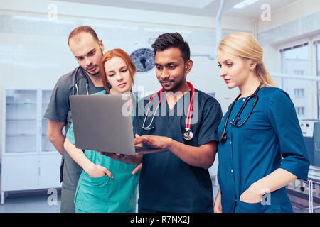 Eine Gruppe von jungen Medizinstudenten mit mixed-race Chirurgen untersucht diese Vorgänge in einem Laptop. Stockfoto