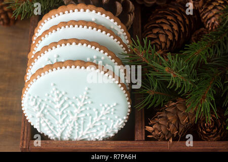 Lebkuchen mit einer Schneeflocke auf einem blauen Hintergrund in eine Holzkiste mit Tannenzweigen und Kegel. Im rustikalen Stil. Stockfoto