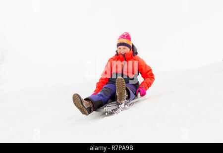 Mädchen Gleiten auf Schnee Untertasse Schlitten im Winter Stockfoto