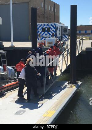 Coast Guard Station Hatteras Inlet Crew Mitglieder und lokale EMS Personal tragen einen verletzten Mann die Rampe hinauf März 23, 2017, an der Station Hatteras Inlet, Hatteras, NC. Die Küstenwache medevaced der 19 Jahre alte Mann aus dem Fischereifahrzeug wenig Jesse nach wurde es berichtet er Verletzungen an der Schulter und Arm in der Nähe von Hatteras Inlet erlitten hatte. Stockfoto