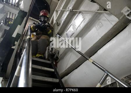 7. US-Flotte von Operationen (27. März 2017) der Bootsmann Mate Seemann Allen Kirkpatrick, von Colorado Springs, Colorado, trägt ein Wasserschlauch unten eine Leiter in einem Hauptraum brandschutzübung an Bord Ticonderoga-Klasse geführte-missile Cruiser USS Lake Champlain (CG57). Lake Champlain ist in regelmäßigen Western Pacific Bereitstellung mit der Carl Vinson Carrier Strike Group als Teil der US-Pazifikflotte-Initiative die Befehls- und Steuerfunktionen der USA 3 Flotte in der Indo-Asia zu verlängern - Pazifik Region. Navy Flugzeugträger Streik Gruppen haben die Indo-Asia-Pazifi patrouillierten Stockfoto