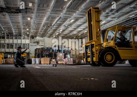 SAN DIEGO (Mar. 30, 2017) Kulinarische Specialist 3. Klasse Rachael Perryman führt den Bediener des Gabelstaplers im Hangar Bucht der Flugzeugträger USS Theodore Roosevelt (CVN 71). Theodore Roosevelt ist derzeit günstig und Naval Air Station North Island homeported. Stockfoto