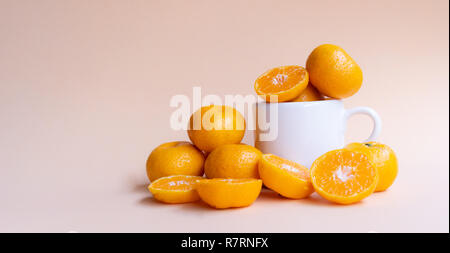 Ganze und halbe schneiden frische Orangen mit weißer Keramik Becher auf weiche Creme Hintergrund Stockfoto