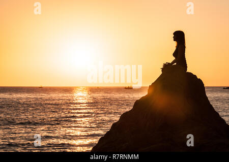 Argelès-sur-Mer (Frankreich). Jemand Yoga auf den Felsen vor der Racou Strand bei Sonnenaufgang. Schöne junge Frau mit braunen Stockfoto