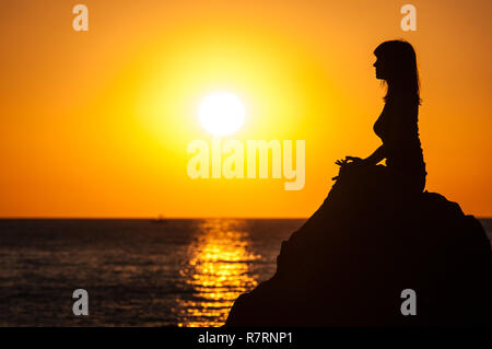 Argelès-sur-Mer (Frankreich). Jemand Yoga auf den Felsen vor der Racou Strand bei Sonnenaufgang. Schöne junge Frau mit braunen Stockfoto