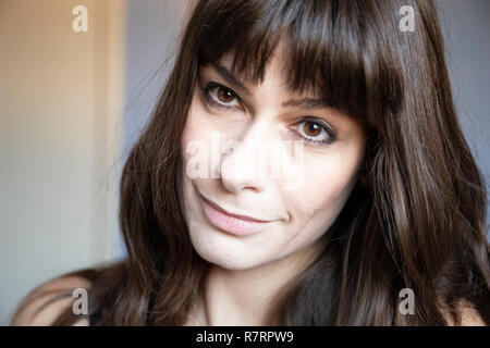 Junge Frau Nahaufnahme Porträt. Kaukasische mit braunen langen Haaren und Pony. Lächelnd Ausdruck, den Kopf schief. Stockfoto