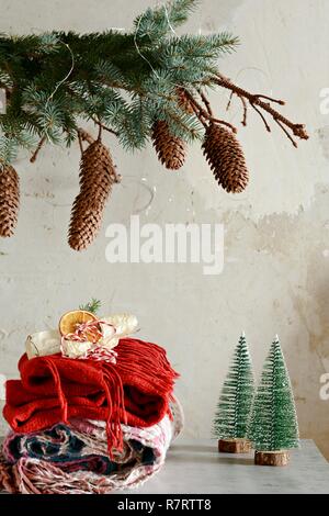 Ein Haufen warme Kleidung auf dem Tisch. Weihnachtliche Atmosphäre im Haus. Zimmer mit Tannenzweigen mit Kegeln eingerichtet. Life style. Herbst oder Winter Stil Stockfoto