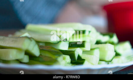 Schneiden Gurken Sticks auf eine weiße Platte. Kann verwendet werden, Salate oder Hosomaki, Gurke Sushi Rollen, oder Kappa Maki zu machen. Verschwommen Küche Hintergrund. Stockfoto