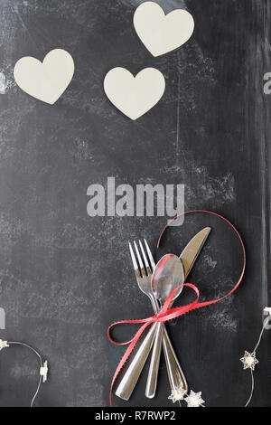 Draufsicht der Valentinstag Dinner Tischdekoration mit Besteck über eine rustikale Tafel Hintergrund mit hölzernen ausgeschnittenen Herzen und Lichterketten. Stockfoto