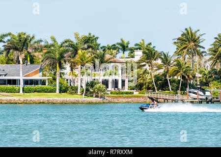 Neapel, USA - 30. April 2018: Nelson's Walk Haus Gebäude mit Wasser auf Dollar Bay, Palmen, blauer Himmel in der Wohngemeinschaft, die Menschen auf dem Boot in Stockfoto