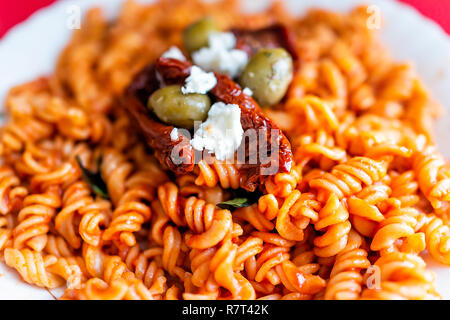 Nahaufnahme von frischen leuchtend rote getrocknete Tomaten Sauce Fusilli glutenfreie Nudeln auf dem Teller in marinara mit Feta Käse, grüne Oliven in Restauran Stockfoto