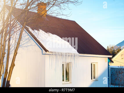 Das kleine Haus mit Eiszapfen. Wohnhaus an einem Wintertag, ein wenig Schnee auf dem Dach in der Sonne, horizontal gedreht. Feder Stockfoto