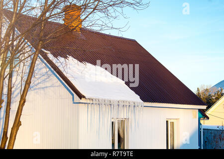 Das kleine Haus mit Eiszapfen. Wohnhaus an einem Wintertag, ein wenig Schnee auf dem Dach in der Sonne, horizontale Schuß Stockfoto