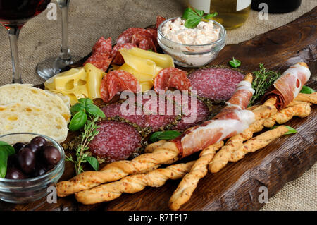 Teller für Antipasti Snacks mit Salami, Brot Sticks (Grissini) mit Schinken, Oliven und Käse Paste auf der Holzoberfläche gewickelt Stockfoto