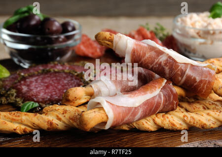 Teller für Antipasti Snacks mit Salami, Brot Sticks (Grissini) mit Schinken, Oliven und Käse Paste auf der Holzoberfläche gewickelt Stockfoto