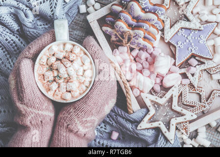 Heiße Schokolade mit Marshmallows Süßigkeiten. Erwärmung Urlaub trinken mit Lebkuchen Cookies. Warme Weihnachten. Weibliche Hände in Handschuhe Holding eine warme Tasse Kakao Verzauberung Stockfoto