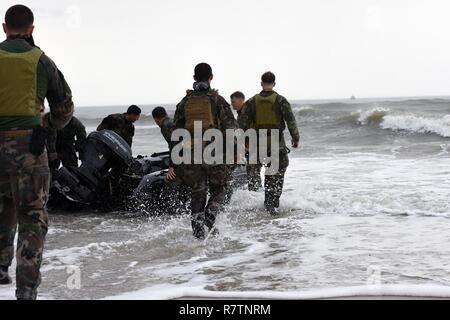 Marines mit Hotel Company, 2 Raider Bataillon, Marine Corps Forces Special Operations Command (MARSOC) in Camp Lejeune in North Carolina, schieben Sie ein Sternzeichen starre Hülle Schlauchboot in die Brandung, während ein 45-Fuß-Antwort Boat-Medium Crew von der Coast Guard Station Wrightsville Beach, North Carolina, bietet Unterstützung von Wasserseite aus Onslow Strand auf Base, 28. März 2017. Station Wrightsville Beach und der Coast Guard Station Emerald Isle Mannschaften regelmäßig partake in Ausbildung Entwicklungen mit MARSOC Einheiten von Camp Lejeune. Stockfoto