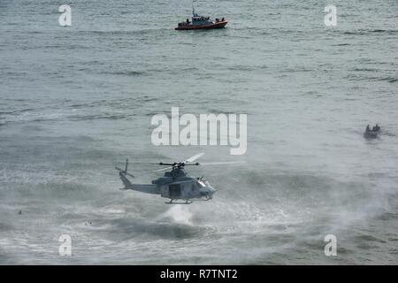 Ein Marine UH-1Y Venom Hubschrauberbesatzung schwebt nach der Bereitstellung von Mitgliedern aus Hotel Company, 2 Raider Bataillon, Marine Corps Forces Special Operations Command (MARSOC) in Camp Lejeune in North Carolina, bei einer gemeinsamen Übung mit der Küstenwache 45-Fuß-Antwort Boat-Medium Crew von Station Wrightsville Beach, North Carolina, an der Basis, 28. März 2017. Die Küstenwache boot Mannschaftsräumen waterside unterstützen, während die Marines mehrfach vom Hubschrauber und schwamm ans Ufer sprang. Stockfoto