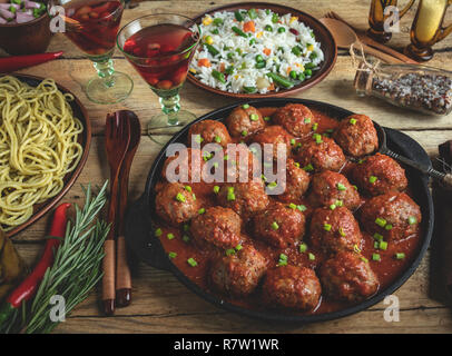 Hausgemachte Frikadellen in Tomatensoße. Pfanne auf einer hölzernen Oberfläche, Reis mit Gemüse, Pasta Stockfoto