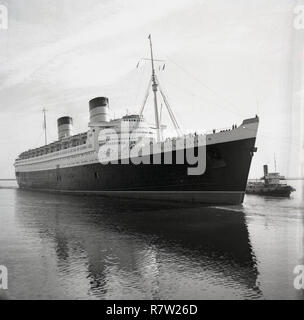 1950, historische, die RMS Queen Elizabeth in Dock von einem schubschiff gebracht. Das dampfschiff war ein Passagierschiff, die ein Luxus Liner service bewtween Southampton und New York City in den USA zur Verfügung gestellt, über Cherbourg in Frankreich. Von John Brown & Co in Clydebank, Schottland, wenn im Jahr 1938 gestartet, war sie das größte Passagierschiff, das jemals gebaut wurde und so für 56 Jahre blieb. Sie wurde als Truppentransporter im Zweiten Weltkrieg verwendet. Stockfoto